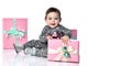 Toddler in gray suit and boots. She smiling, posing with pink decorated gift boxes, sitting on floor isolated on white. Close up Royalty Free Stock Photo