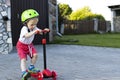 Toddler in a helmet rides a red scooter in the yard Royalty Free Stock Photo