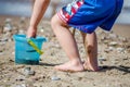 Toddler Kid Play with his Bucket on the Sundy Beach. Happy Boy Fills the Bucket with Sand and Water. Child Plays by the Sea Royalty Free Stock Photo