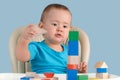 Toddler 12-17 months building a tower of colored wooden cubes sitting on a child`s chair, on a blue background Royalty Free Stock Photo