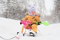 Toddler 12-17 months old with a green toy shovel in his hands sits on a children`s snowcat in a winter park Royalty Free Stock Photo