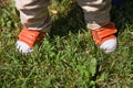 Toddler`s legs in orange sneakers standing on grass. Top view on baby`s feet. Summer background. outdoors