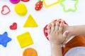 Toddler sculpts from colored plasticine on a white table.