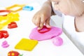 Toddler sculpts from colored plasticine on a white table.