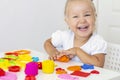 Toddler sculpts from colored plasticine on a white table.