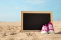 Toddler shoes and mini chalk board on the sand, beach concept ba