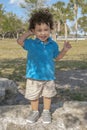 A toddler stands upon a large rock at the park looking at the camera
