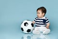 Toddler in striped t-shirt, white pants and booties. He is looking up, sitting on floor against blue background. Close up Royalty Free Stock Photo