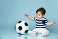 Toddler in striped t-shirt, white pants and booties. He is looking up, sitting on floor against blue background. Close up Royalty Free Stock Photo