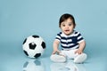 Toddler in striped t-shirt, white pants and booties. He is looking up, sitting on floor against blue background. Close up Royalty Free Stock Photo