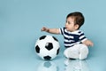 Toddler in striped t-shirt, white pants and booties. He is looking up, sitting on floor against blue background. Close up Royalty Free Stock Photo