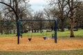 Toddler swings in city park with park bench, person walking and birds and squirrel and a few cars in the background - selective fo Royalty Free Stock Photo