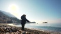 Toddler throwing pebble in sea on stony coast