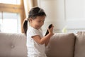 Toddler vietnamese girl sit on couch holding smartphone watching cartoons