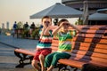 Toddlers boy and his sibling brother sitting on a bench by the c