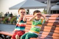 Toddlers boy and his sibling brother sitting on a bench by the c