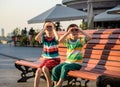 Toddlers boy and his sibling brother sitting on a bench by the city