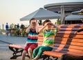 Toddlers boy and his sibling brother sitting on a bench by the city