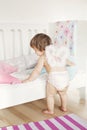 Todler baby girl in nappy and angel wings plays near bed. Interior design of children`s room in light colors