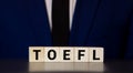 Toefl word concept on cubes with wooden model on blue background