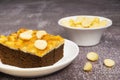 Toffee chocolate cake slice with macadamia seeds at above for dessert break, nuts in white bowl for background Royalty Free Stock Photo