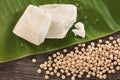 Tofu on green leaf with drops and soybeans on wood background.