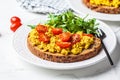 Tofu scramble toast with tomatoes and arugula on white plate, white marble background. Vegan food concept