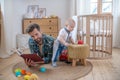 Father in a checkered shirt layng on the floor and reading a book, his little son playing next to him