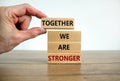 Together we are stronger symbol. Wooden blocks with words `together we are stronger`. Male hand. Beautiful wooden table, white