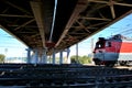 Bottom view of an automobile overpass and a diesel locomotive passing under it on a bright sunny day.