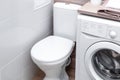 Toilet bowl with a closed chair cover in a bathroom with a washing machine. Compact layout