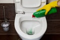 Toilet cleaning and disinfection. Hands in yellow rubber gloves pour disinfectant into the toilet