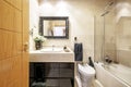 Toilet with light colored marble tiles, veined marble cabinet and black gloss wood base, framed mirror and walk-in shower with Royalty Free Stock Photo