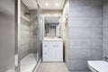 Toilet in modern apartment with shower, screen, white cabinet, toilet and walls covered