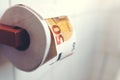 toilet paper roll hanging on wooden holder in tiled bathroom with large banknote between sheets Royalty Free Stock Photo