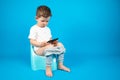 Toilet training. Full-length portrait boy with smartphone sitting on the pot on isolated blue Royalty Free Stock Photo