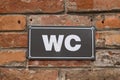 Toilet WC sign on old red brick wall. White WC sign on black metal plate. Outdoor sign. Royalty Free Stock Photo