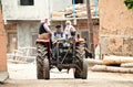 A farmer driving his tractor in the middle of a village. Two women riding with him Royalty Free Stock Photo