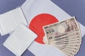 Cloth masks and 100,000 yen cash sent by govt to fight COVID-19 on Japan flag background.