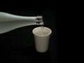 Pouring sake, liquor made from rice, from glass bottle into a cup on black background Royalty Free Stock Photo
