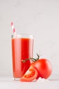 Tomato beverage in glass with branch tomatoes, straw, salt and juicy slice on white wood table, closeup, vertical. Royalty Free Stock Photo