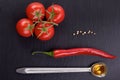 Tomato bunch, chili pepper, grains of white pepper, spoon of olive oil on dark stone