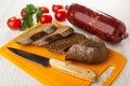 Tomato, parsley, smoked sausage, slices of bread, knife on plastic cutting board on wooden table Royalty Free Stock Photo