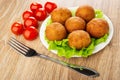 Tomato cherry, white plate with small fried pies on leaves lettuce, fork on table Royalty Free Stock Photo