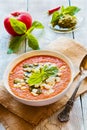 Tomato cream soup with feta cheese and pesto sauce in white bowl on wooden background. Fresh basil leaves