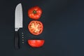 A tomato cut into two halves with a sharp knife. Circles of red tomatoes with knife on black background. Harvesting tomatoes.