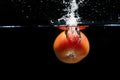 Tomato falling into the water and splashing drops on black background