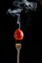 Tomato on fork with steam on black background