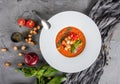 Tomato gazpacho soup with basil, croutons, herbs and vegetables on grey background, Spanish cuisine.