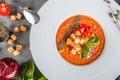Tomato gazpacho soup with basil, croutons, herbs and vegetables on grey background, Spanish cuisine.
